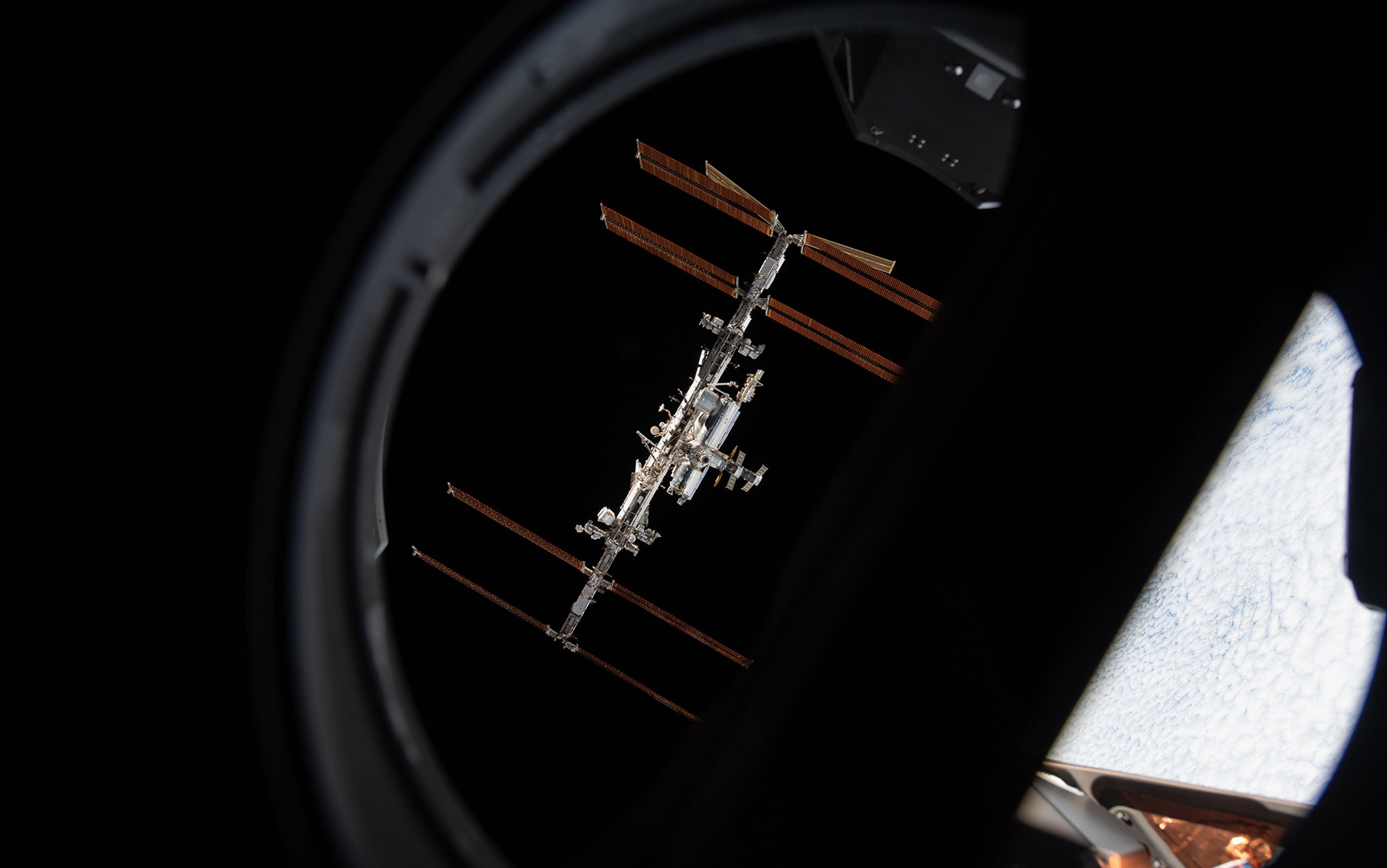 The International Space Station is seen at an angle through a window against the darkness of space